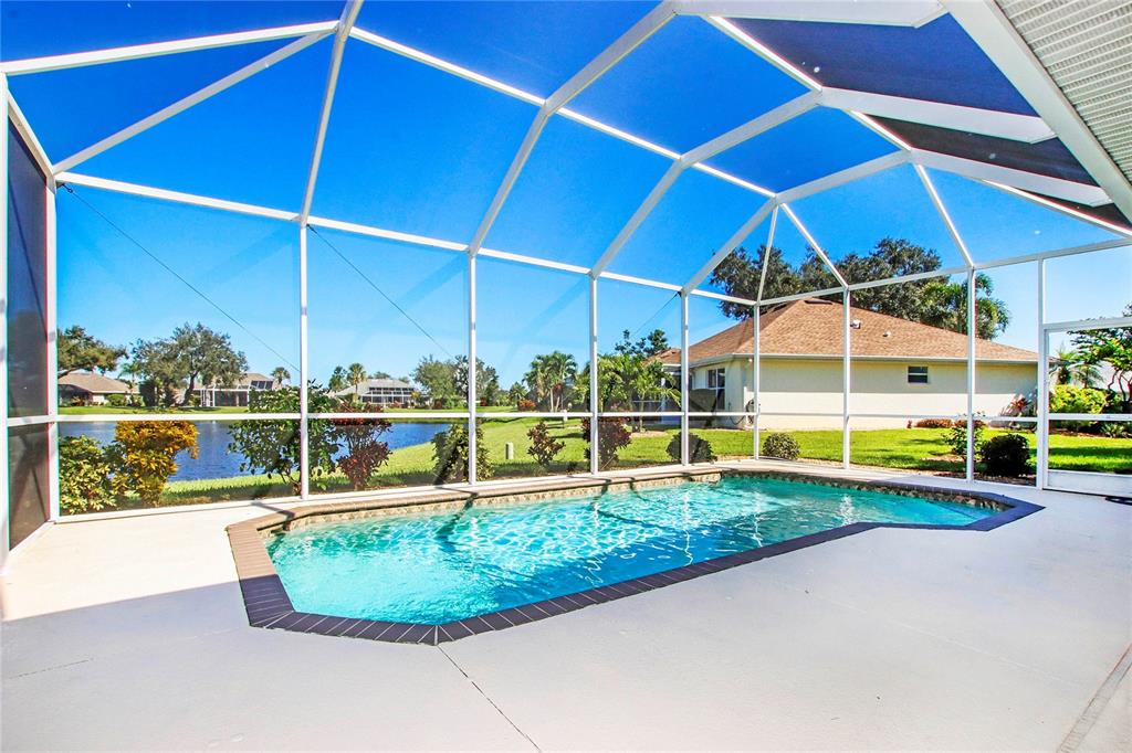 A swimming pool enclosed by a white screen cage overlooks a lake and neighboring houses — 2525 JASMINE WAY, NORTH PORT, FL