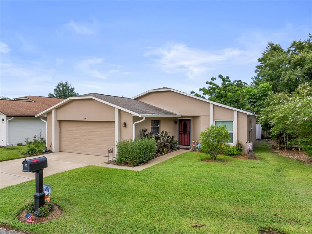 A single-story house with a tan stucco exterior, a two-car garage, and a front lawn — 112 MAYFAIR CT, SANFORD, FL