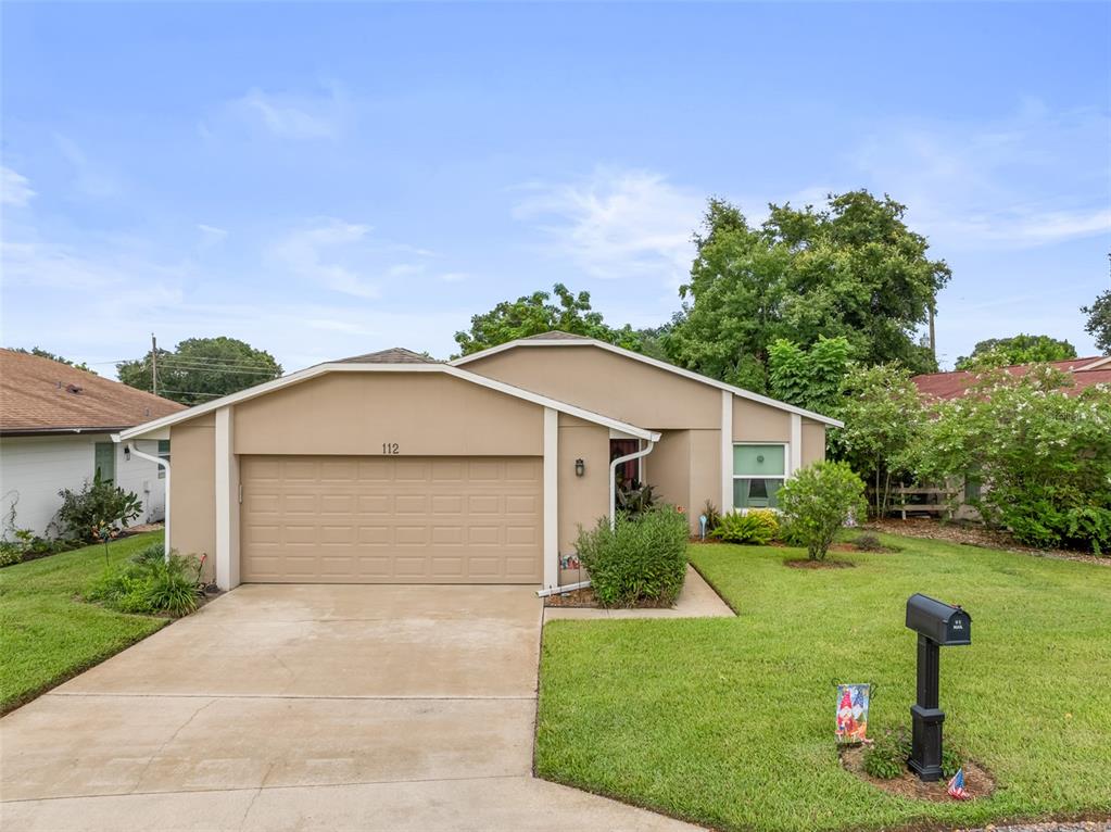 A single-story house with a beige exterior, a two-car garage, and a front lawn — 112 MAYFAIR CT, SANFORD, FL