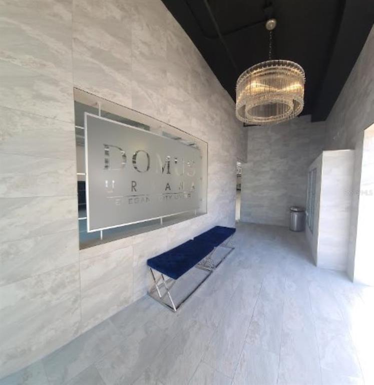 A modern lobby features light gray tiled walls, a blue velvet bench, and a crystal chandelier — 644 3RD AVENUE S UNIT 408, ST PETERSBURG, FL
