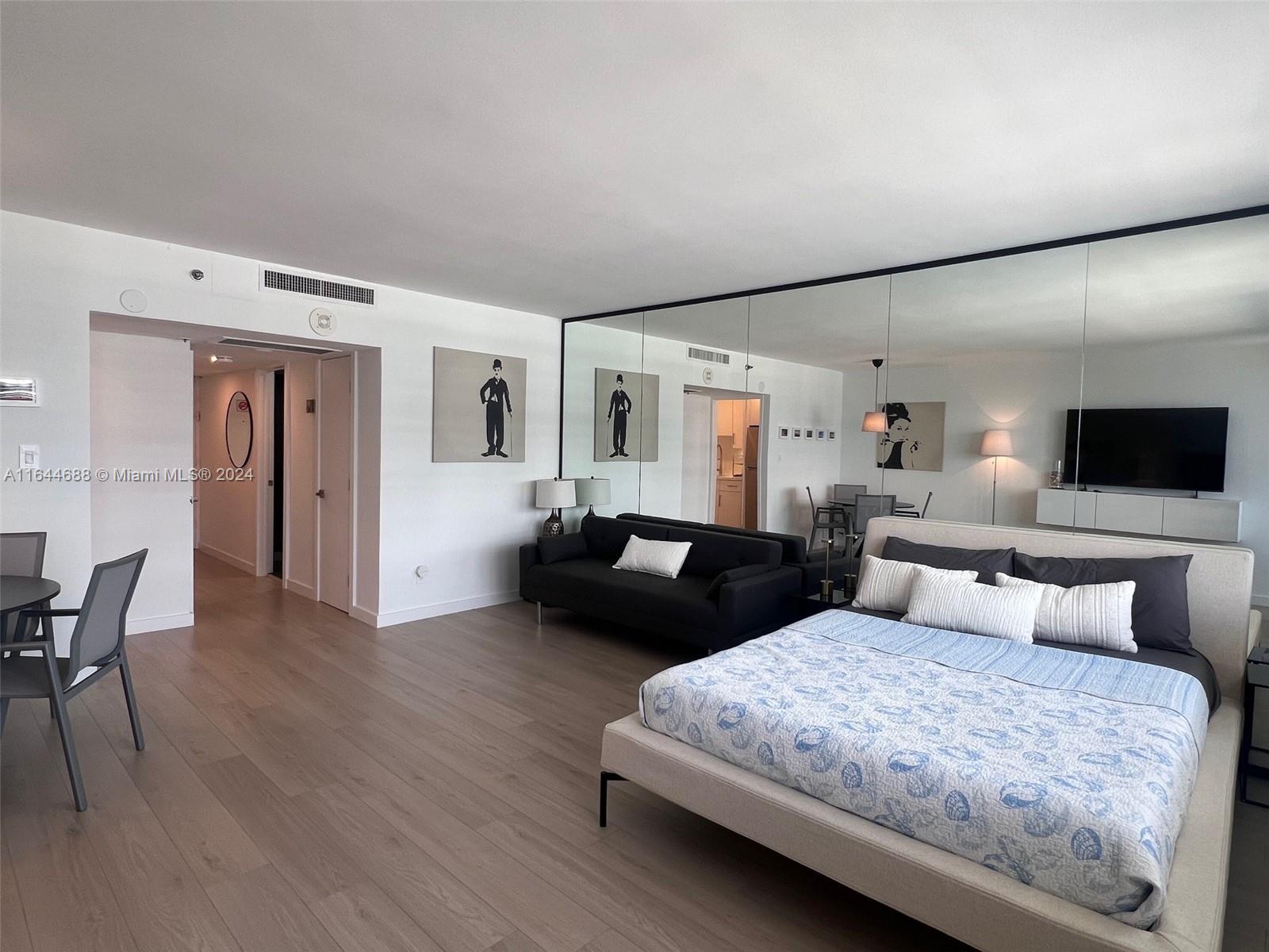 A bedroom features light wood flooring, a large bed, a black sofa, and mirrored walls — 100 Lincoln Rd # 1104, Miami Beach FL 33139, MIAMI BEACH, FL