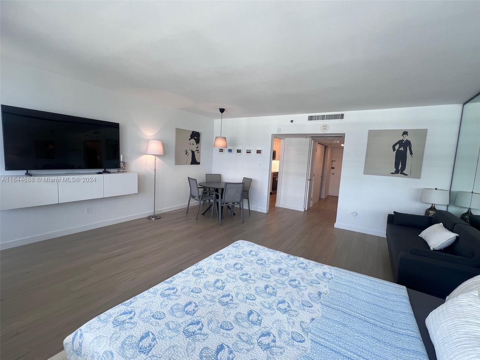 A bedroom with a bed, a dining area, a television, and light wood flooring — 100 Lincoln Rd # 1104, Miami Beach FL 33139, MIAMI BEACH, FL