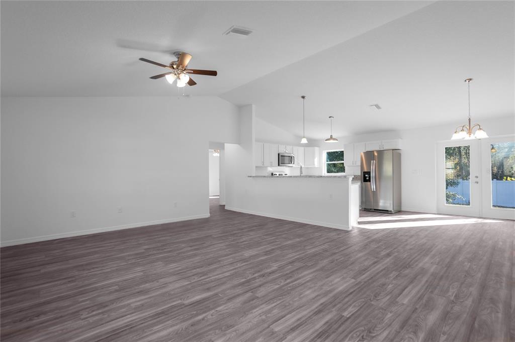 An open-concept living room and kitchen with white walls and grey wood-look flooring — 729 DRAKE AVENUE, INVERNESS, FL