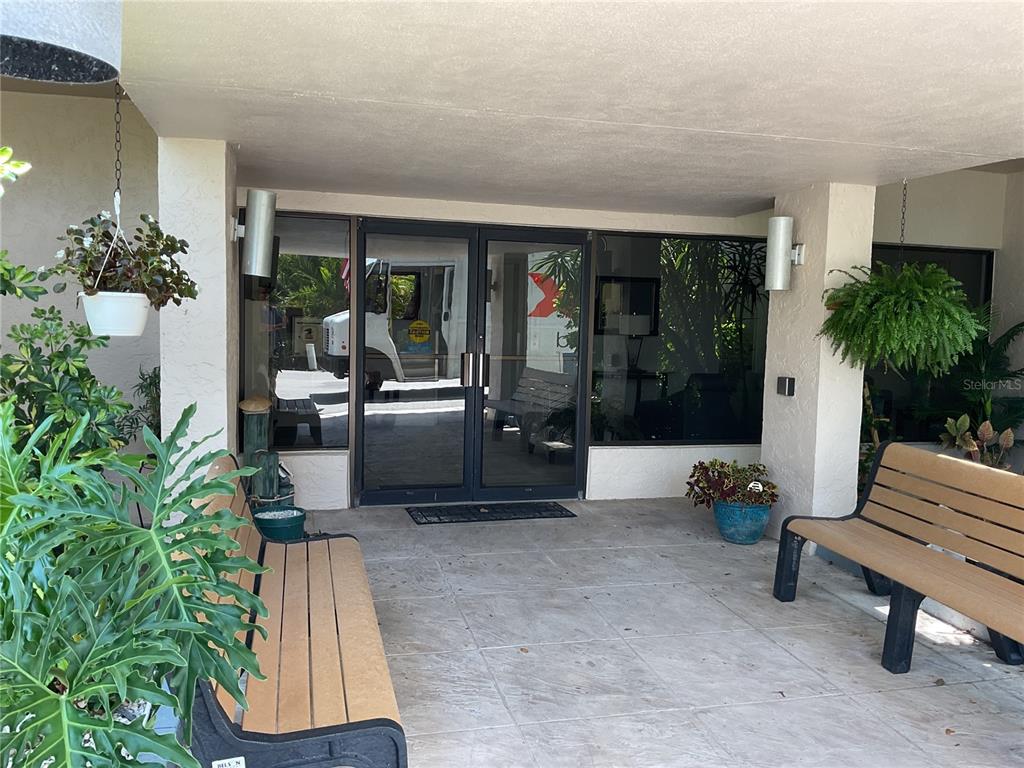 A covered building entrance features glass double doors, two benches, and potted plants — 25188 MARION AVENUE UNIT D207, PUNTA GORDA, FL