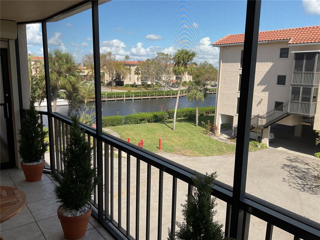 A screened-in balcony overlooks a canal, grassy lawn, and a neighboring apartment building — 25188 MARION AVENUE UNIT D207, PUNTA GORDA, FL