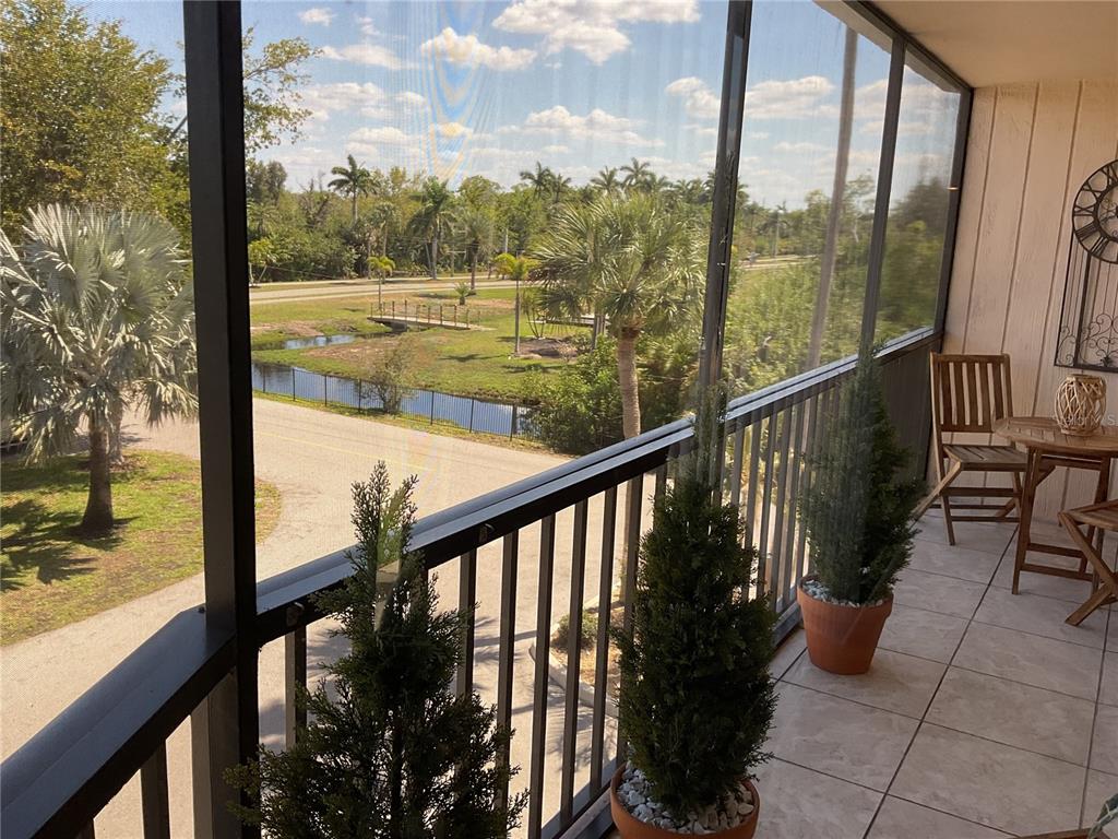 A screened-in balcony overlooks a road, a small canal, and palm trees — 25188 MARION AVENUE UNIT D207, PUNTA GORDA, FL