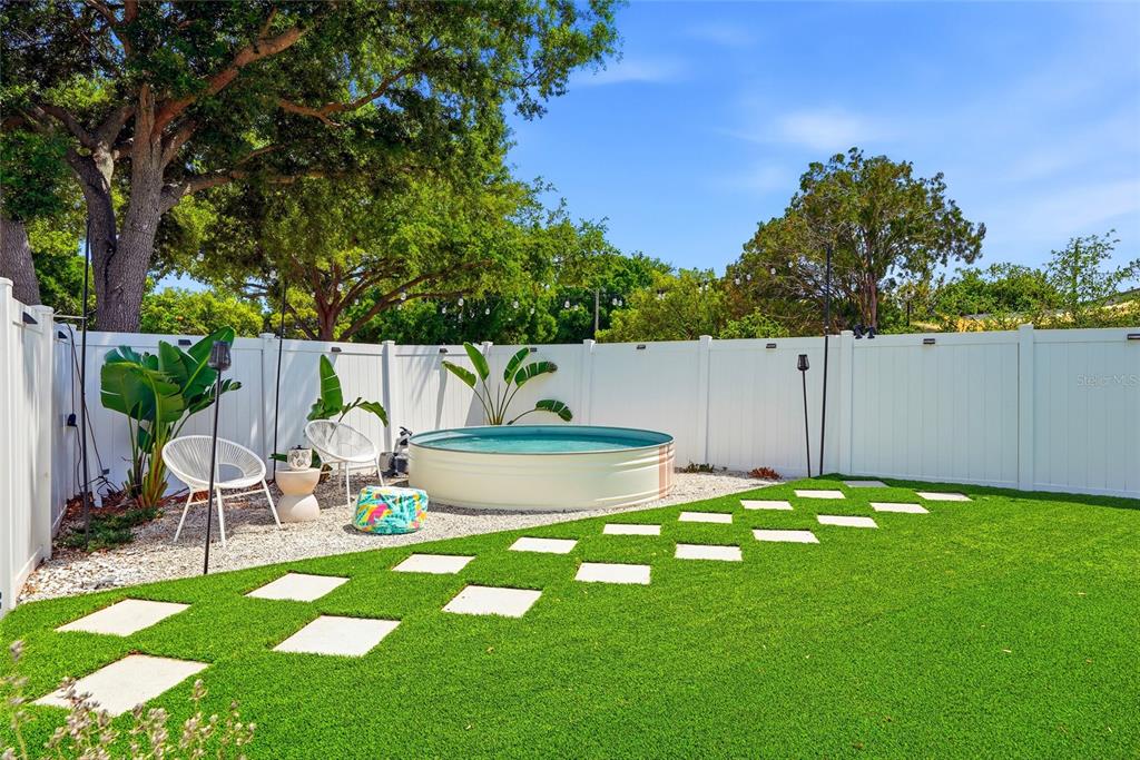 A backyard features a round stock tank pool, white vinyl fencing, and artificial turf grass — 1134 MEADOWLAWN DRIVE N, ST PETERSBURG, FL