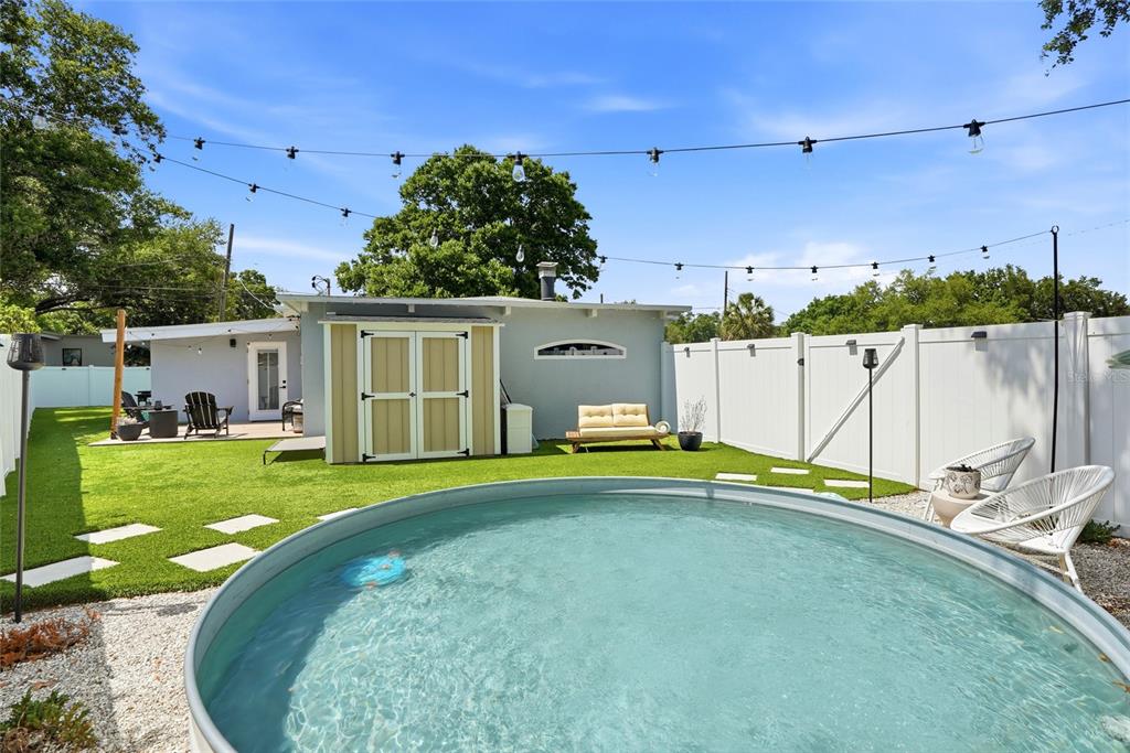 A backyard features a round stock tank pool, artificial turf, a storage shed, and string lights — 1134 MEADOWLAWN DRIVE N, ST PETERSBURG, FL