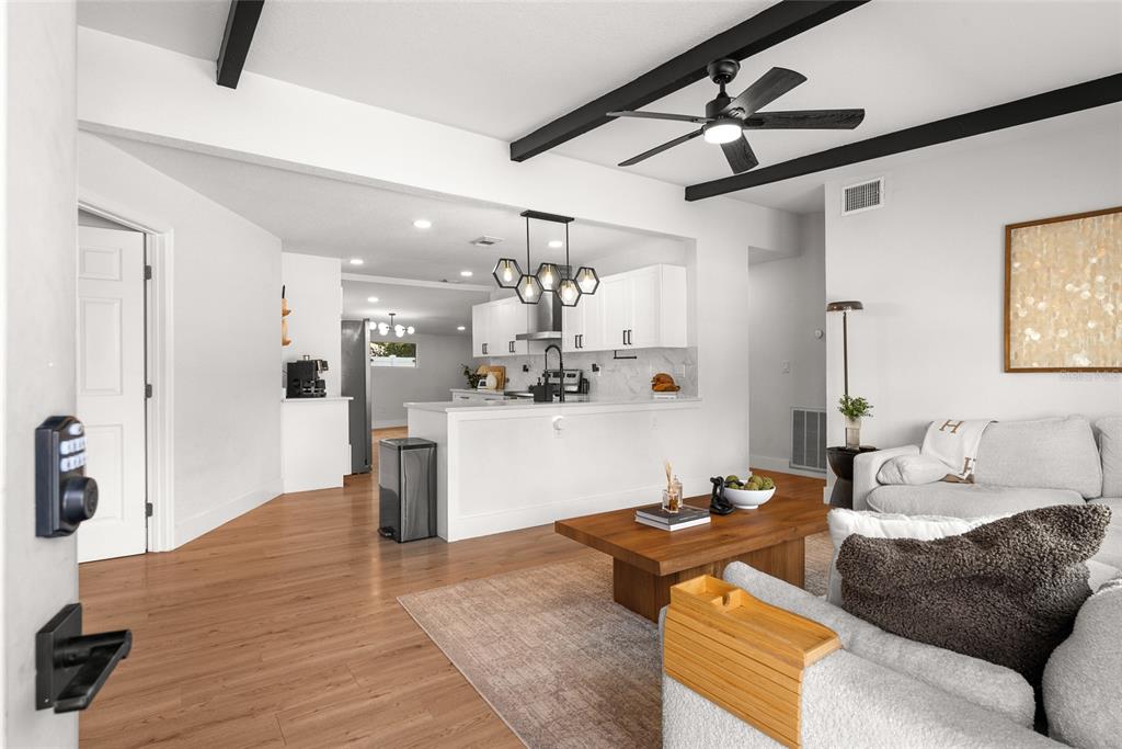 A living room with wood flooring opens to a kitchen featuring white cabinets and island — 1134 MEADOWLAWN DRIVE N, ST PETERSBURG, FL