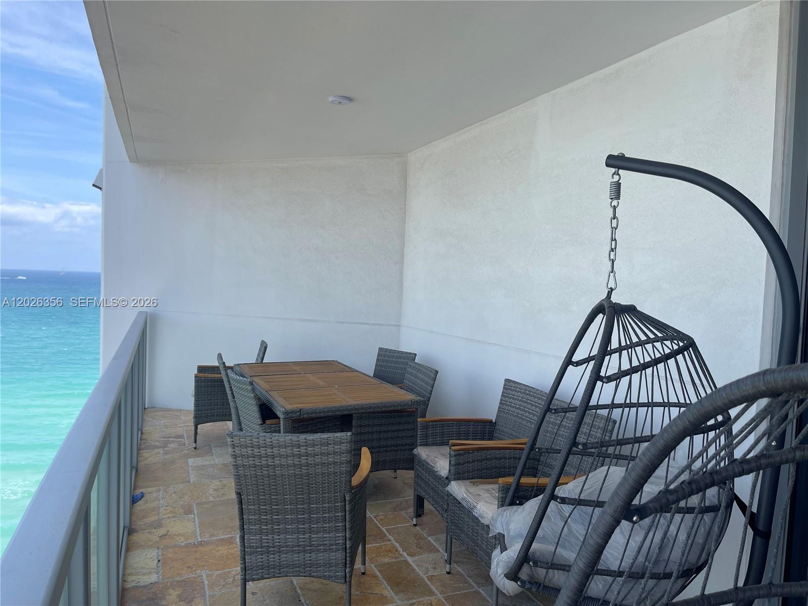 A balcony features a dining set, a hanging chair, and a view of the ocean — 3101 S Ocean Dr # 1707, Hollywood FL 33019, HOLLYWOOD, FL