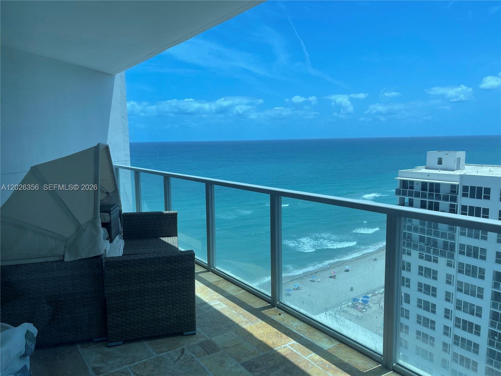 A balcony with wicker furniture overlooks the ocean and a neighboring high-rise building — 3101 S Ocean Dr # 1707, Hollywood FL 33019, HOLLYWOOD, FL