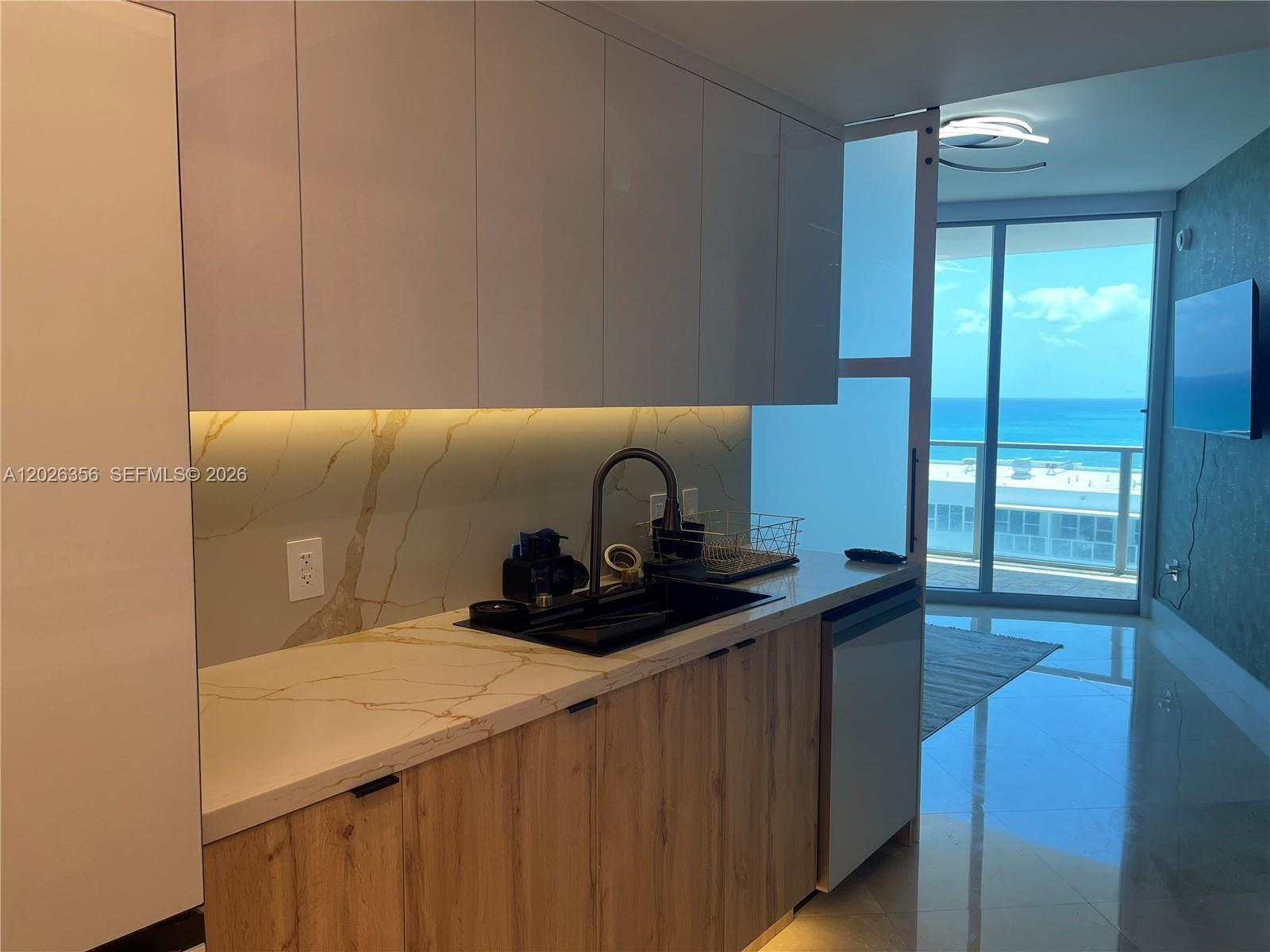 A modern kitchenette features wood-grain cabinets, marble-patterned countertops, and a view of the ocean — 3101 S Ocean Dr # 1707, Hollywood FL 33019, HOLLYWOOD, FL