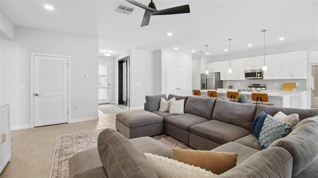 A modern open-concept living room features a large gray sectional sofa and a white kitchen — 61 BEAUFORD LANE, PALM COAST, FL