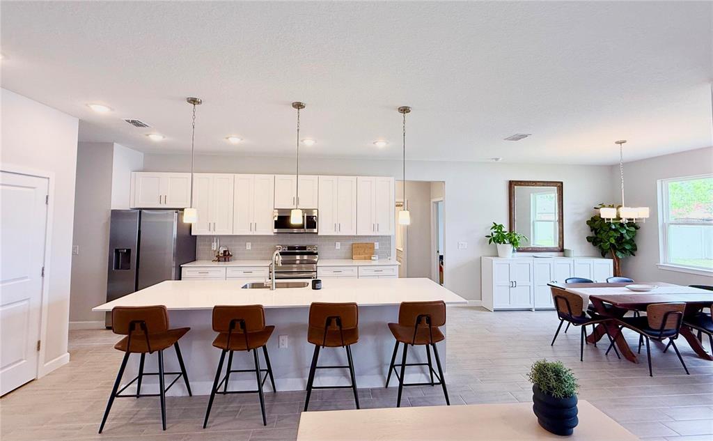 A modern kitchen features white cabinetry, a large quartz island, and an adjacent dining area — 61 BEAUFORD LANE, PALM COAST, FL