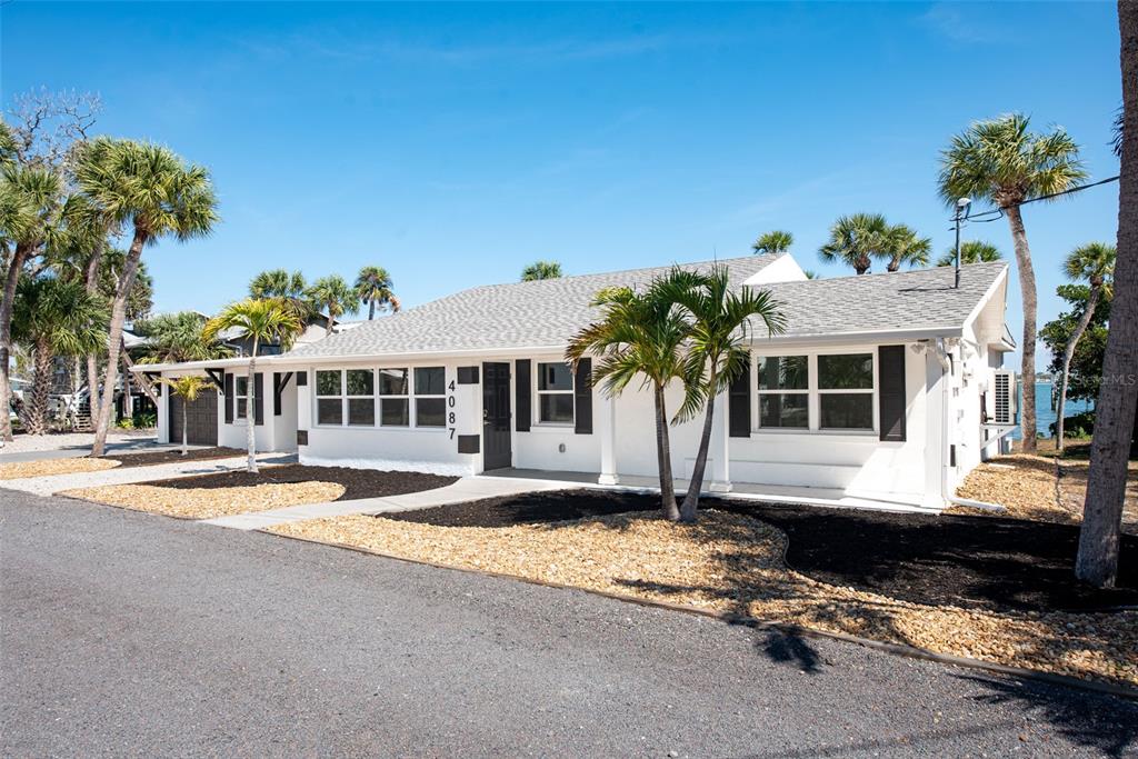 A white single-story house with a gray shingled roof and palm trees in the yard — 4087 PELICAN SHORES CIRCLE, ENGLEWOOD, FL