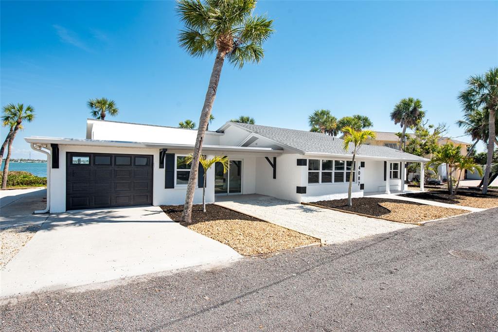 A white, single-story house with a dark garage door and palm trees in the yard — 4087 PELICAN SHORES CIRCLE, ENGLEWOOD, FL