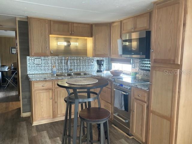 A kitchen sink area features oak cabinets, granite countertops, and a metallic patterned backsplash — 800 32ND AVENUE S UNIT 227, ST PETERSBURG, FL