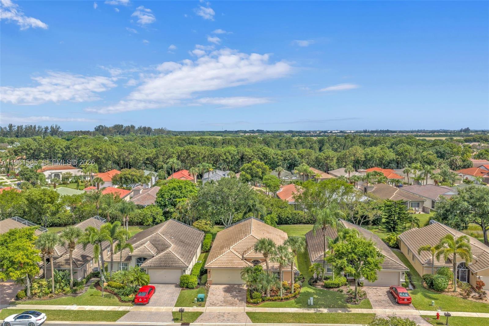 An aerial view shows a suburban neighborhood with single-family homes, palm trees, and green landscaping — 8046 Duomo Cir, Boynton Beach FL 33472, BOYNTON BEACH, FL