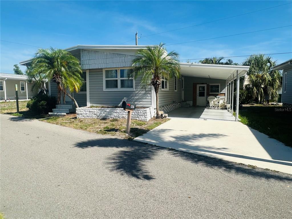A single-story manufactured home with grey siding, a white brick planter, and two palm trees — 147 MAUI DRIVE, PALMETTO, FL
