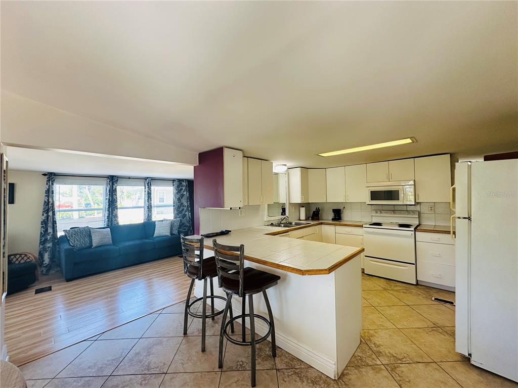 An open-concept kitchen with white cabinets and a breakfast bar overlooks a living room — 147 MAUI DRIVE, PALMETTO, FL