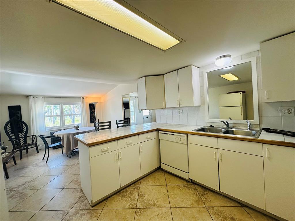 A kitchen with white cabinets, tiled countertops, and a dining area in the background — 147 MAUI DRIVE, PALMETTO, FL