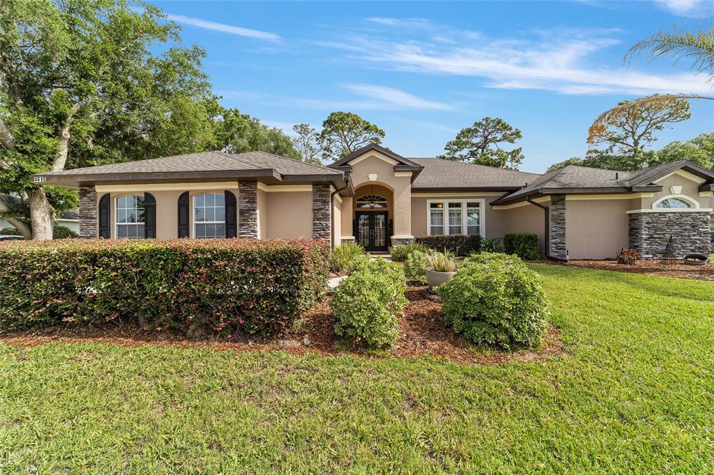 A single-story house with a tan stucco exterior, stone accents, and a dark shingled roof — 4615 SE 35TH PLACE, OCALA, FL