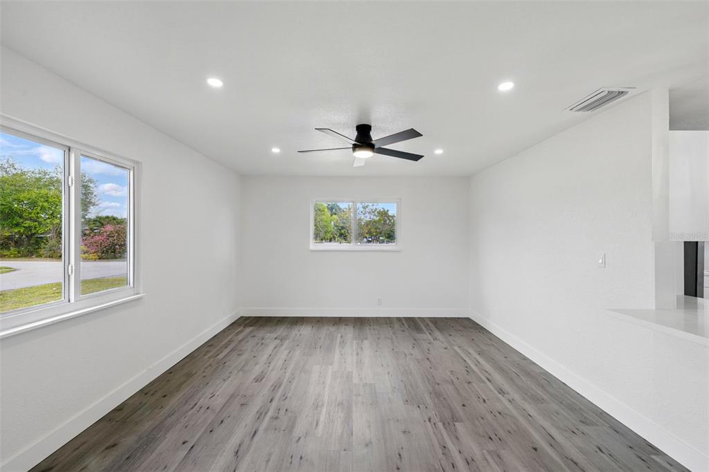 A bright, empty room features white walls, gray wood-look flooring, and a ceiling fan — 1867 NW 8TH AVENUE, HOMESTEAD, FL