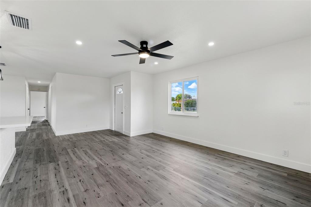 A bright, empty room features white walls, gray wood-look flooring, and a black ceiling fan — 1867 NW 8TH AVENUE, HOMESTEAD, FL