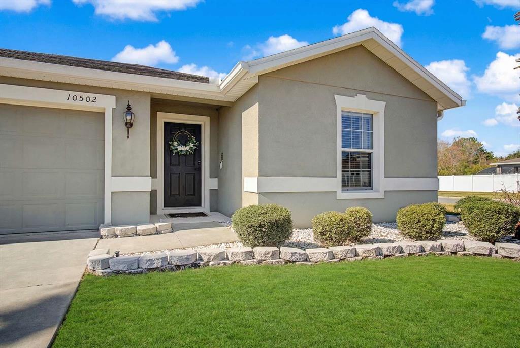 A single-story house exterior features a gray stucco facade, a black front door, and landscaping — 10502 BULL GRASS DRIVE, ORLANDO, FL