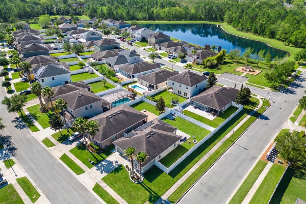 An aerial view shows a suburban neighborhood with houses, swimming pools, and a nearby lake — 10502 BULL GRASS DRIVE, ORLANDO, FL