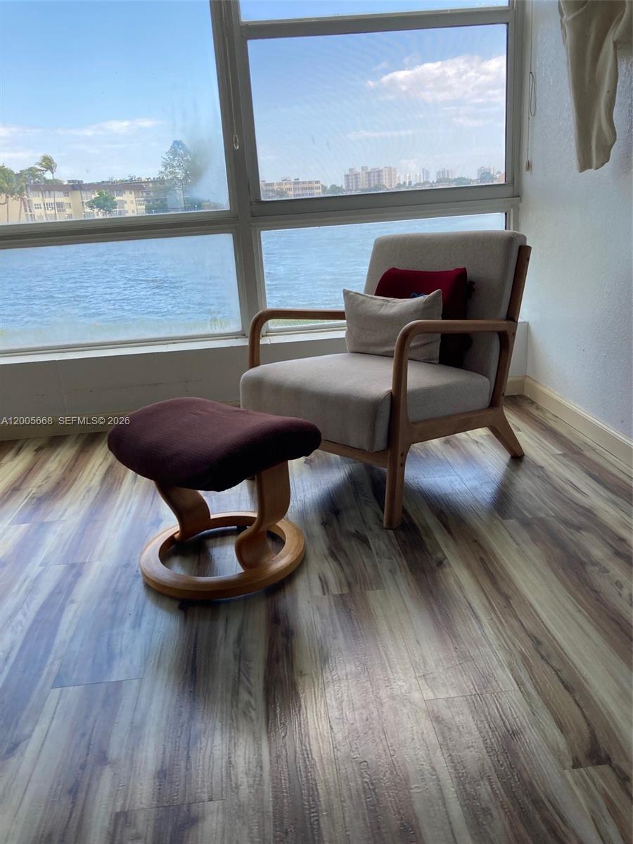 A light-colored armchair and matching ottoman sit on wood-look flooring before a waterfront window — 18901 NE 14th Ave # 101, Miami FL 33179, MIAMI, FL