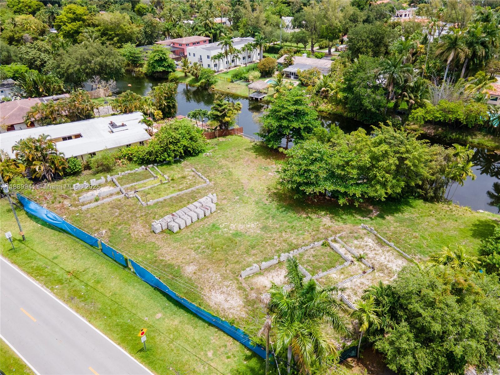 An aerial view shows a vacant lot with concrete foundation footings and stacked building blocks — 11595 W Biscayne Canal Rd, Miami FL 33161, MIAMI, FL