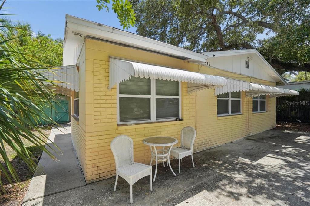 A yellow brick exterior wall features white metal awnings over windows and a small patio — 526 12TH AVENUE S, ST PETERSBURG, FL