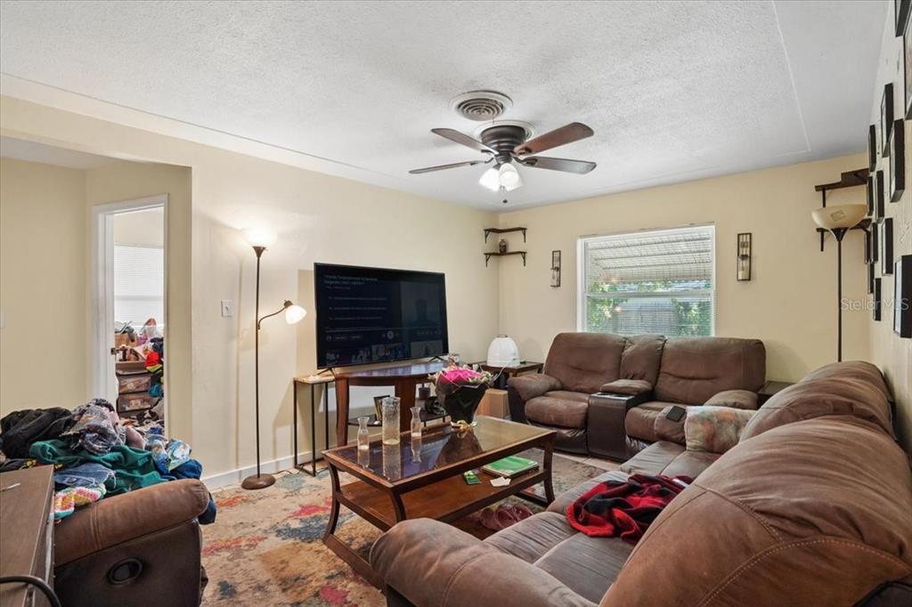 A living room features brown reclining sofas, a coffee table, a television, and patterned carpeting — 526 12TH AVENUE S, ST PETERSBURG, FL