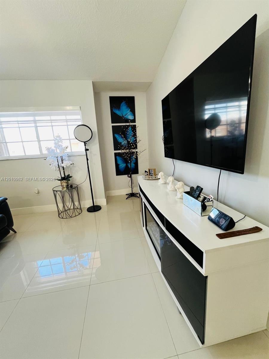 A living room features a large wall-mounted television, a white media console, and butterfly wall art — 7817 W 36th Ave # 204, Hialeah FL 33018, HIALEAH, FL