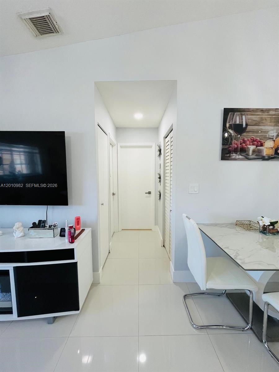 A hallway with white tile floors connects a living area to a closed door — 7817 W 36th Ave # 204, Hialeah FL 33018, HIALEAH, FL
