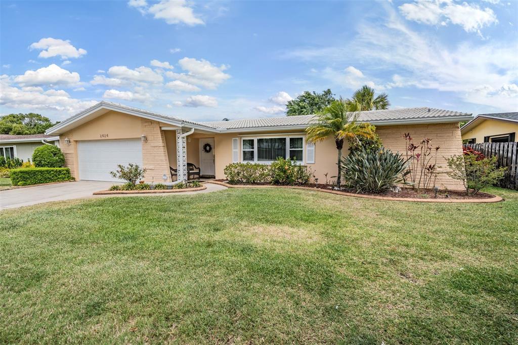 A single-story house exterior features a white garage door, an American flag, and landscaping — 2424 FAIRBANKS DRIVE, CLEARWATER, FL