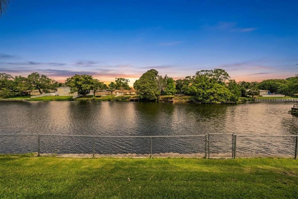 A grassy backyard overlooks a calm lake with trees and houses on the far bank — 2424 FAIRBANKS DRIVE, CLEARWATER, FL