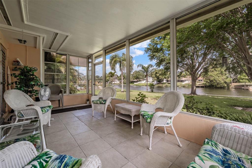 A screened-in porch with tile flooring, wicker furniture, and a view of a lake — 2424 FAIRBANKS DRIVE, CLEARWATER, FL