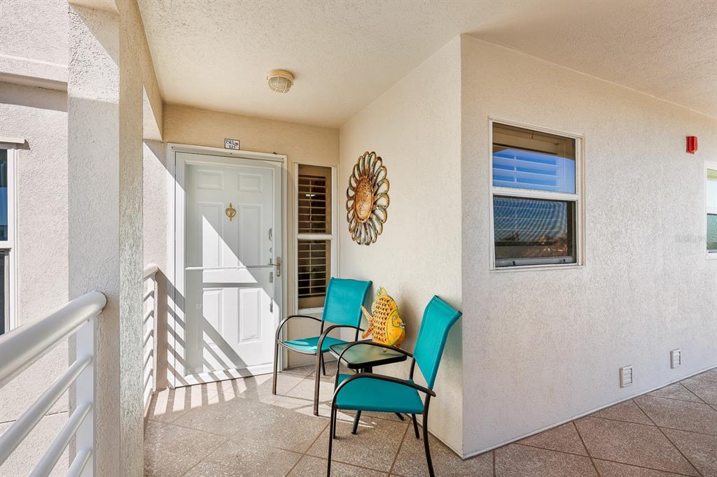 A covered balcony features two teal chairs, a small table, and a white entry door — 5901 BAHIA DEL MAR CIRCLE UNIT 521, ST PETERSBURG, FL