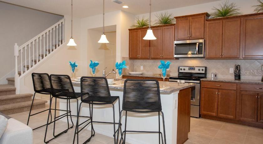 A kitchen features wooden cabinets, a breakfast bar with three stools, and an adjacent staircase — 8879 GENEVE COURT, KISSIMMEE, FL