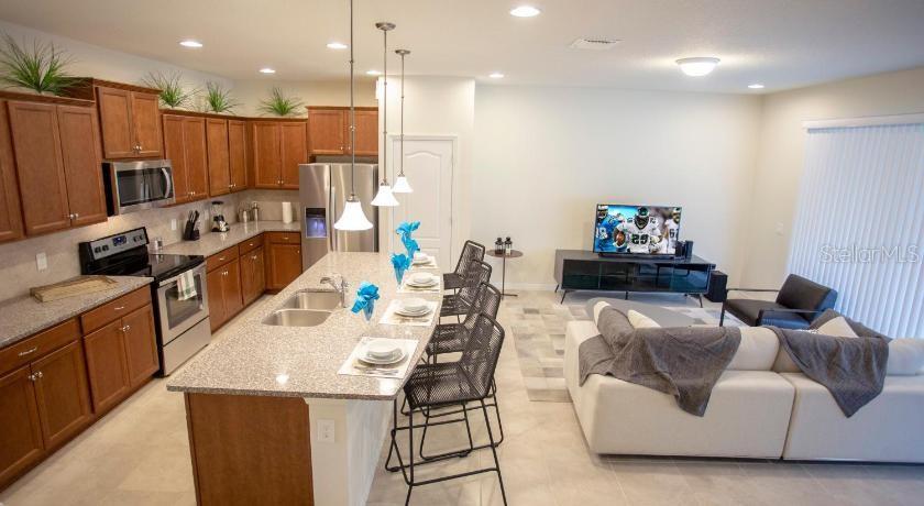 An open-concept kitchen with wood cabinets and granite countertops flows into a living room area — 8879 GENEVE COURT, KISSIMMEE, FL