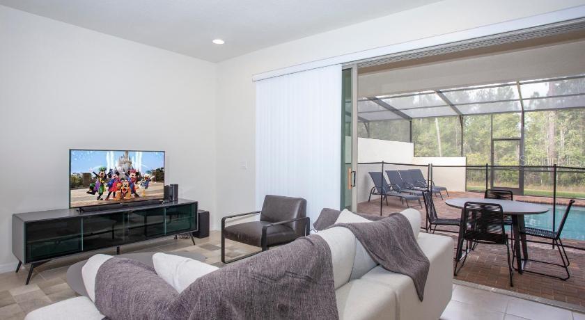 A living room with a television, sofa, and sliding glass doors opening to a pool — 8879 GENEVE COURT, KISSIMMEE, FL