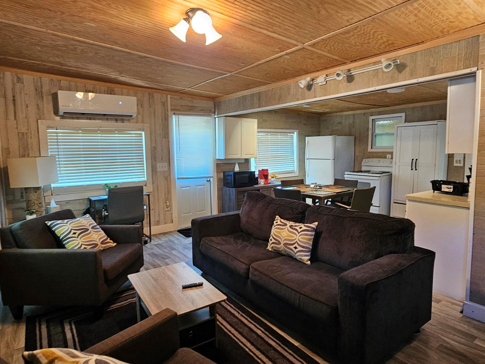 A living room with a dark sofa and chairs, wood-paneled walls, and an open kitchen — 1087 Dusty Lane, Moore Haven FL 33471, MOORE HAVEN, FL