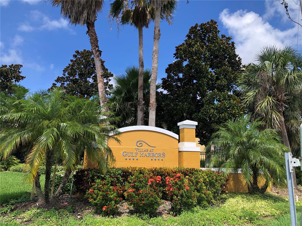 A yellow monument sign for Villas at Gulf Harbors stands amidst palm trees and landscaping — 4704 CASSWELL DRIVE, NEW PORT RICHEY, FL
