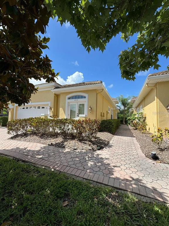 A yellow house with a paved walkway and a small garden under a blue sky — 4704 CASSWELL DRIVE, NEW PORT RICHEY, FL