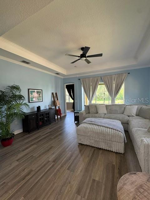 A living room features light blue walls, wood-look flooring, a tray ceiling, and a sectional sofa — 4704 CASSWELL DRIVE, NEW PORT RICHEY, FL