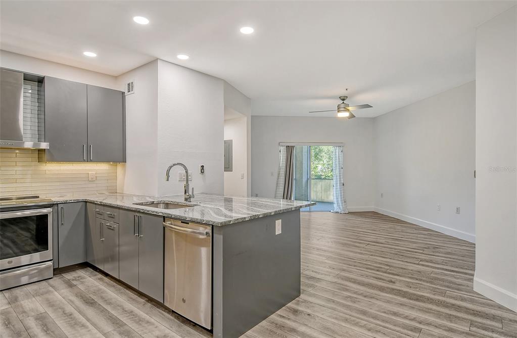 A modern kitchen with gray cabinets and granite countertops opens into a bright living area — 5160 NORTHRIDGE ROAD UNIT 107, SARASOTA, FL