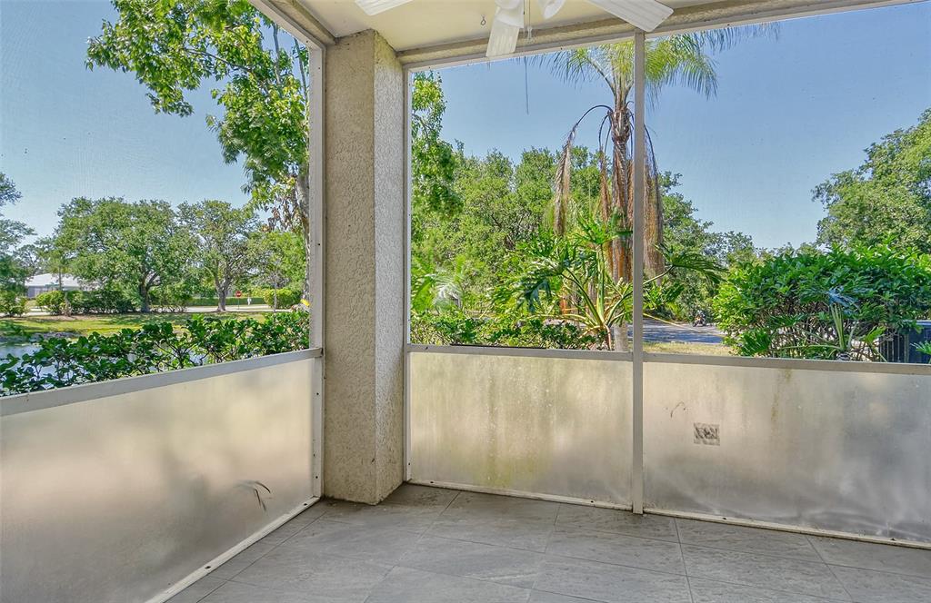 A screened-in porch with tiled flooring overlooks a pond and lush green trees — 5160 NORTHRIDGE ROAD UNIT 107, SARASOTA, FL