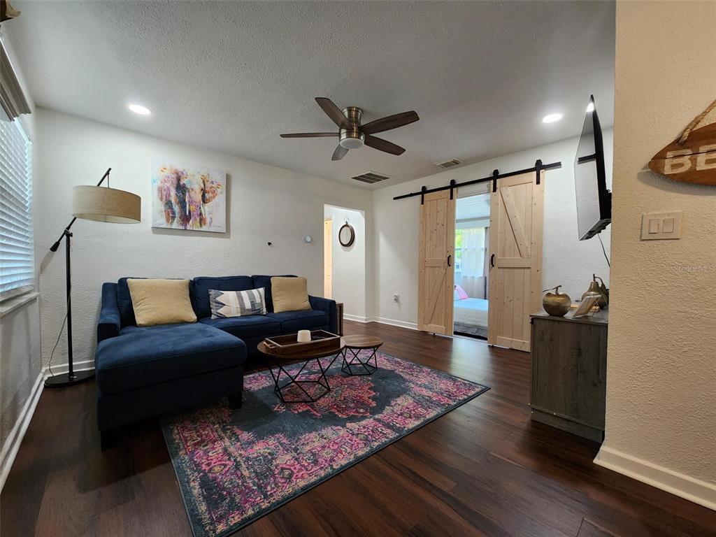 A living room features a blue sectional sofa, a patterned rug, and wooden barn doors — 618 S CREST AVE, CLEARWATER, FL